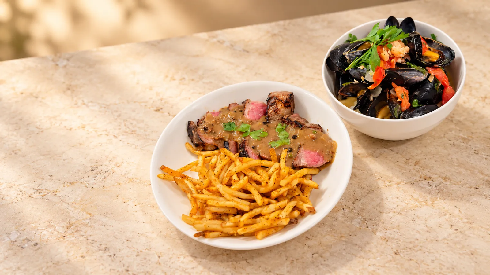 Steak with fries and mussels prepared for a Bow to Plates culinary experience.